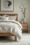 Scandinavian bedroom with a light oak bed frame, neutral bedding, a wooden side table with ceramic vases, and a minimalist black-and-white print above the bed.