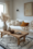A minimalist living room featuring a white linen sofa adorned with neutral and mustard throw pillows, a rustic wooden coffee table, and a textured white and black rug. The space is styled with natural elements, including pampas grass in a ceramic vase, creating a cozy and serene ambiance.