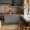 A modern minimalist kitchen with light gray cabinetry, natural stone backsplash, wooden stools, woven baskets, and rustic decor accents.